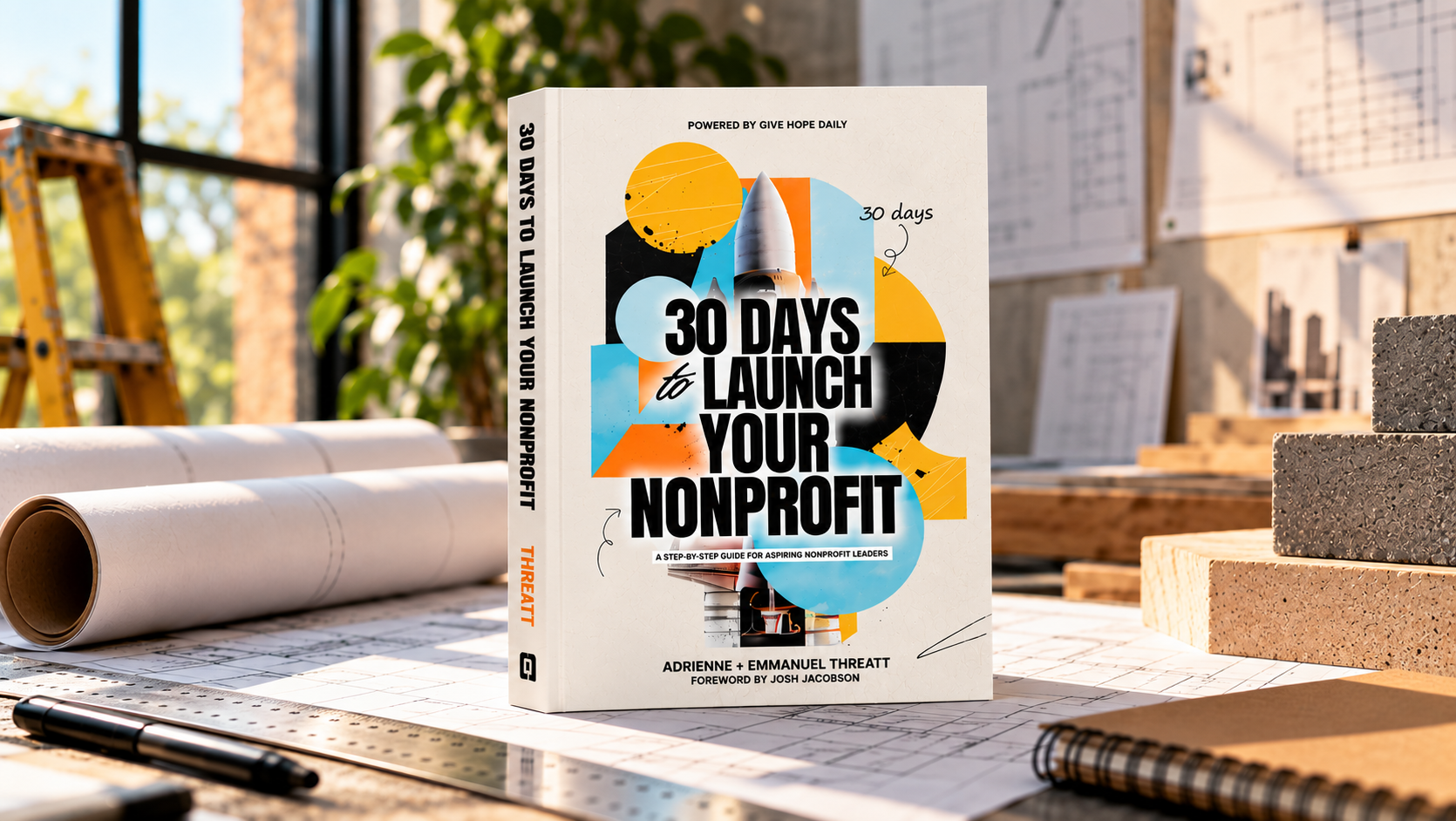 30 Days to Launch Your Nonprofit by Adrienne and Emmanuel Threatt, hardcover book on a drafting table with rolled plans